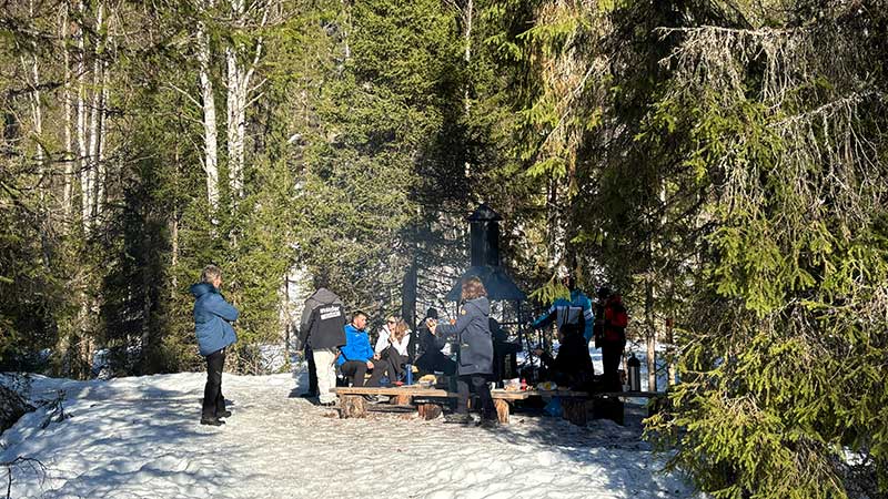 Ihmisiä seisomassa ja istumassa tulentekopaikalla talvella.