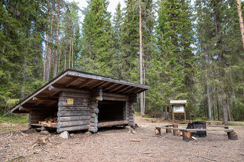 Pyöröhirsistä rakennetun laavun edustalla on tulentekopaikka ja sen ympärissä lankusta tehty istumakehä. Ympärillä on metsää ja metsän reunassa opaste.