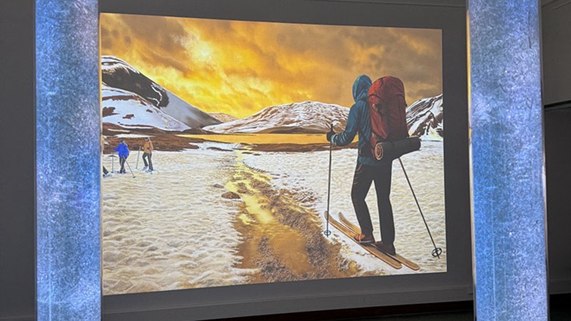 Teos näyttelyssä. Teoksessa hiihtäjiä ja osin sulanutta lunta.