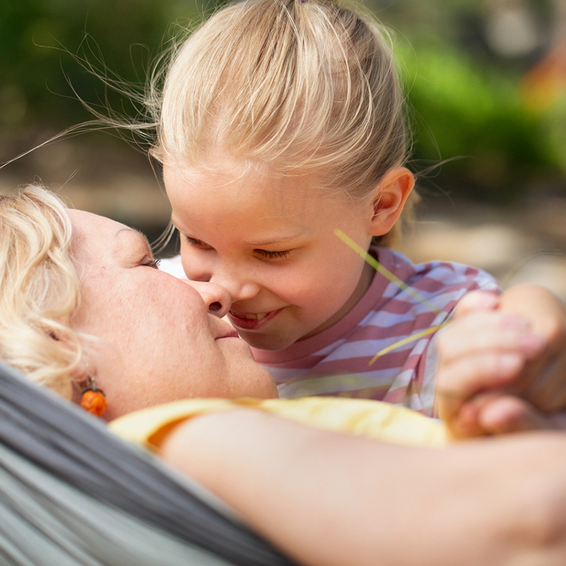 Riippukeinussa makaava nainen ja lapsi hierovat neniään yhteen.