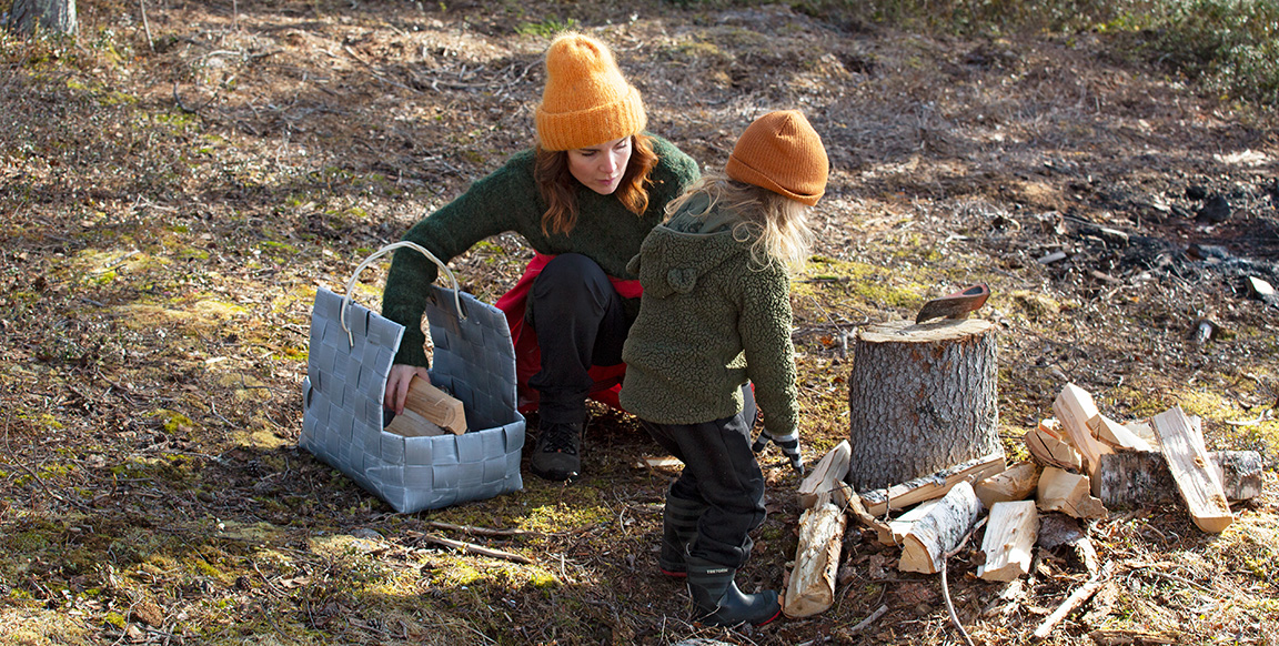 A woman and child collect chopped logs into a basket in the forest.