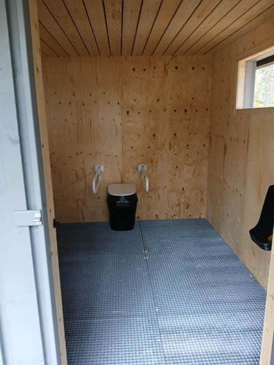 Esteettömän käymäläosaston sisätila, jossa on teräsritilälattiat sekä käsituet käymäläistuimen molemmin puolin.