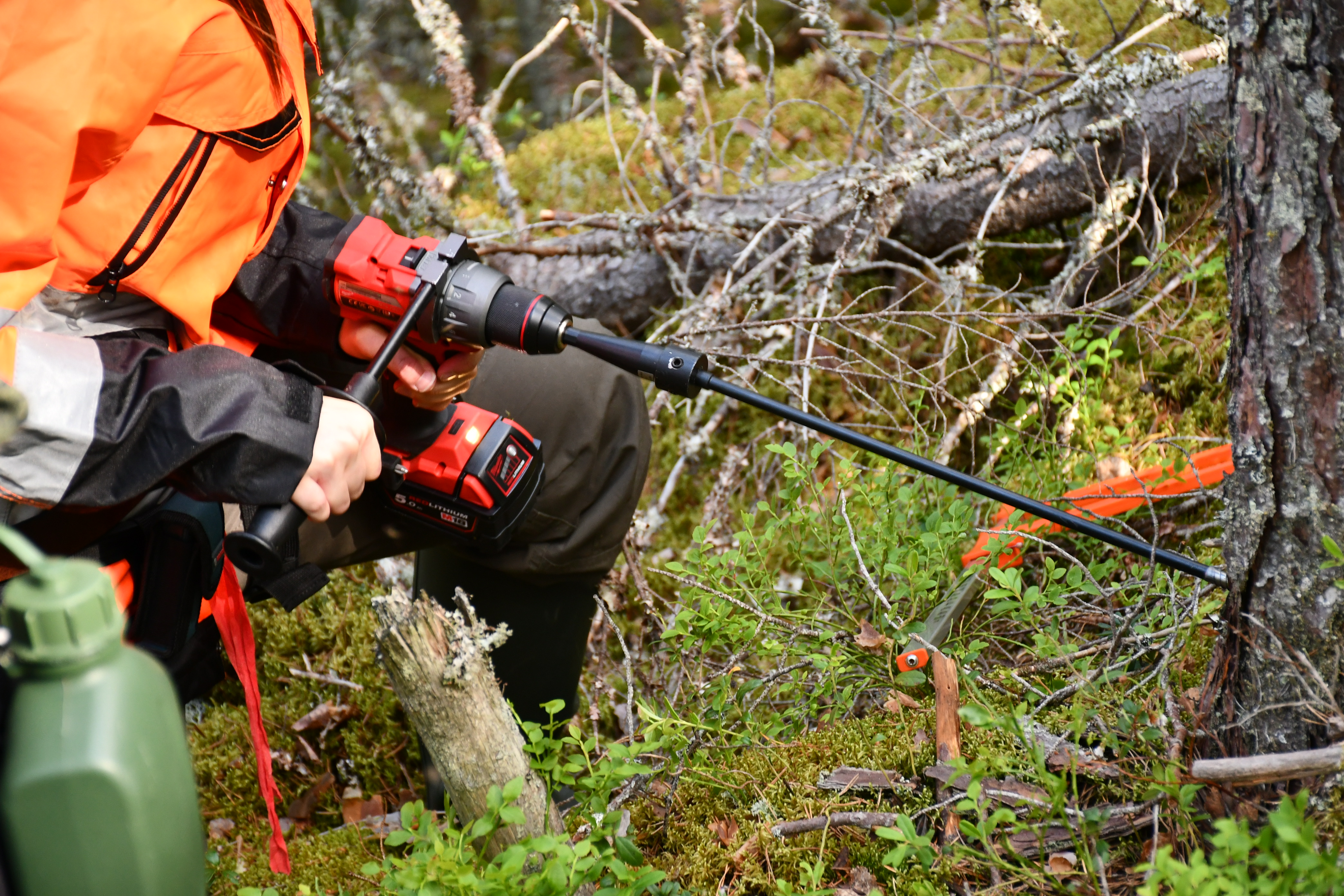 Oranssiasuinen henkilö kairaa puuta metsässä koneella.