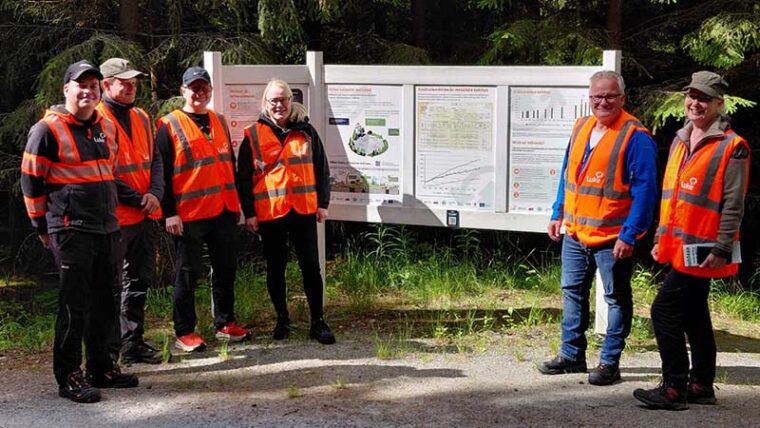 Kuusi huomioliivistä henkilöä maasto-opasteen luona kesällä.